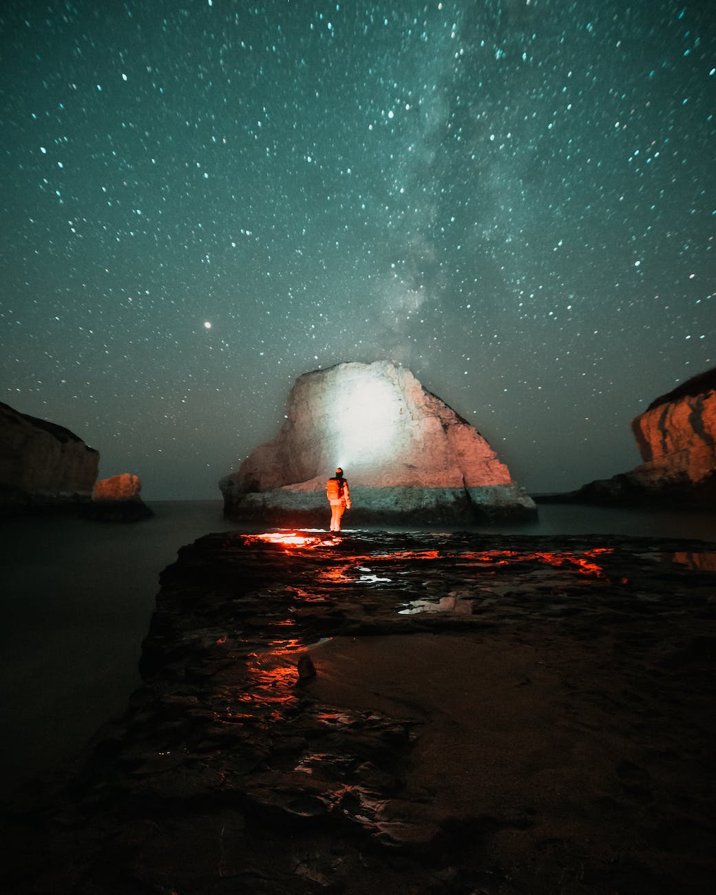 person standing on rock near body of water during night time